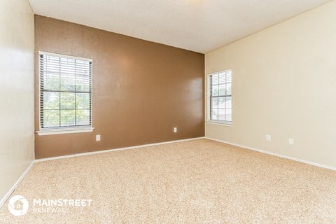 the spacious living room of a townhouse with carpet and two windows
