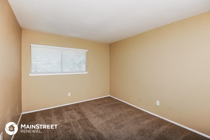 the bedroom of a house with carpet and a window