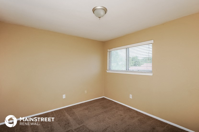 the spacious bedroom with carpeted flooring and a window