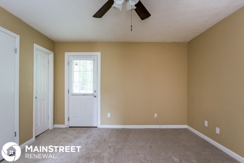 an empty living room with a ceiling fan and a white door