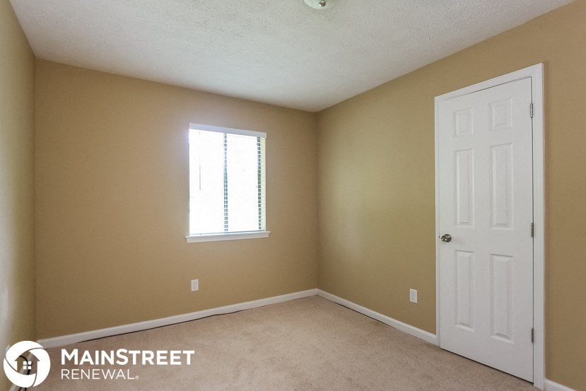 a bedroom with a white door and a window and a carpeted floor