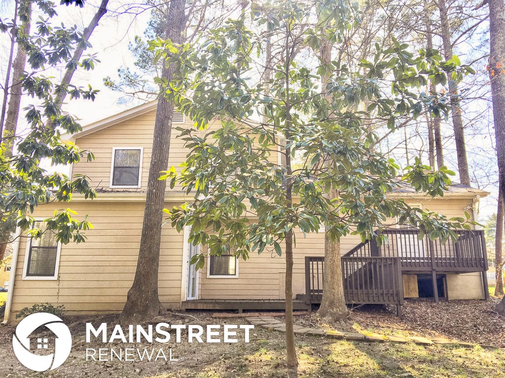 a small yellow house with a deck and trees