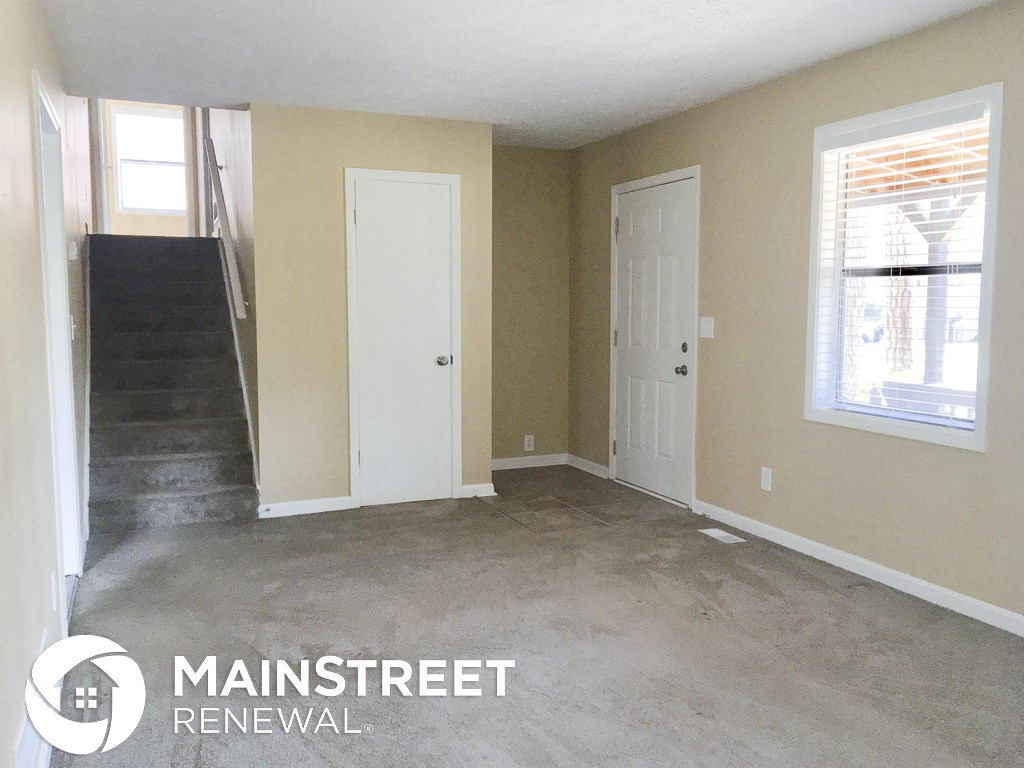 an empty room with a staircase and a white door and a window