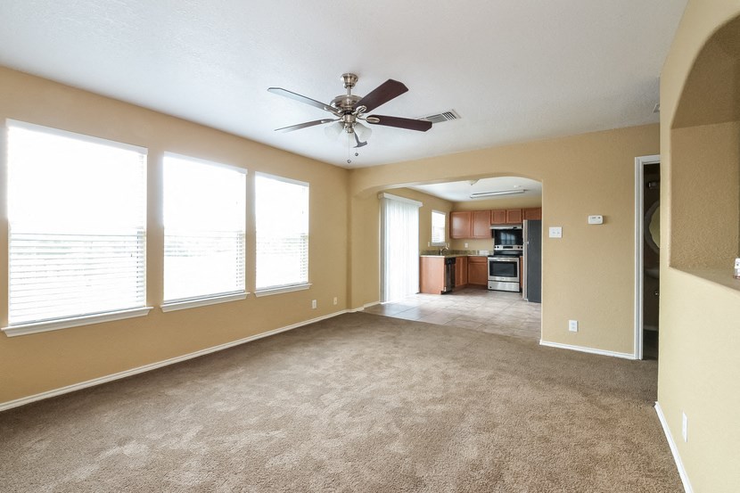 an empty living room with a ceiling fan and large windows