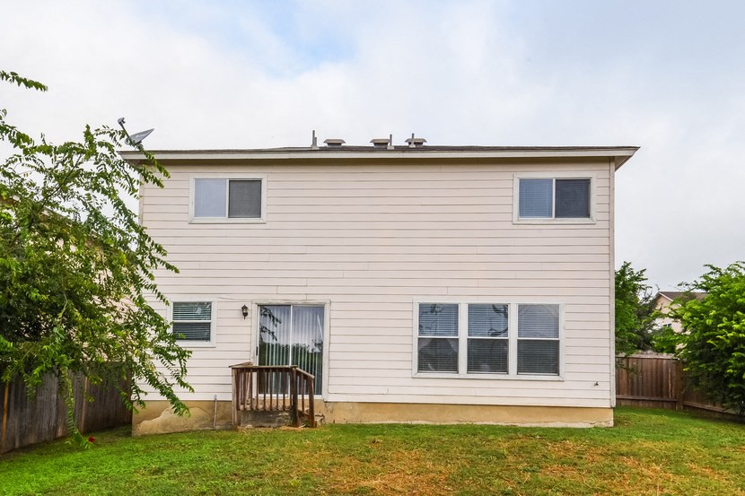 the back of a white house with a yard and a deck