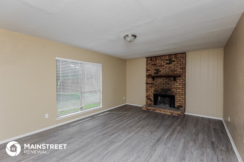 the living room of a home with a brick fireplace and wooden floors