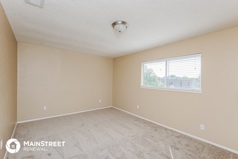 the spacious living room of an apartment with carpet and a window