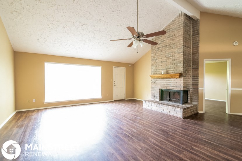an empty living room with a fireplace and a ceiling fan