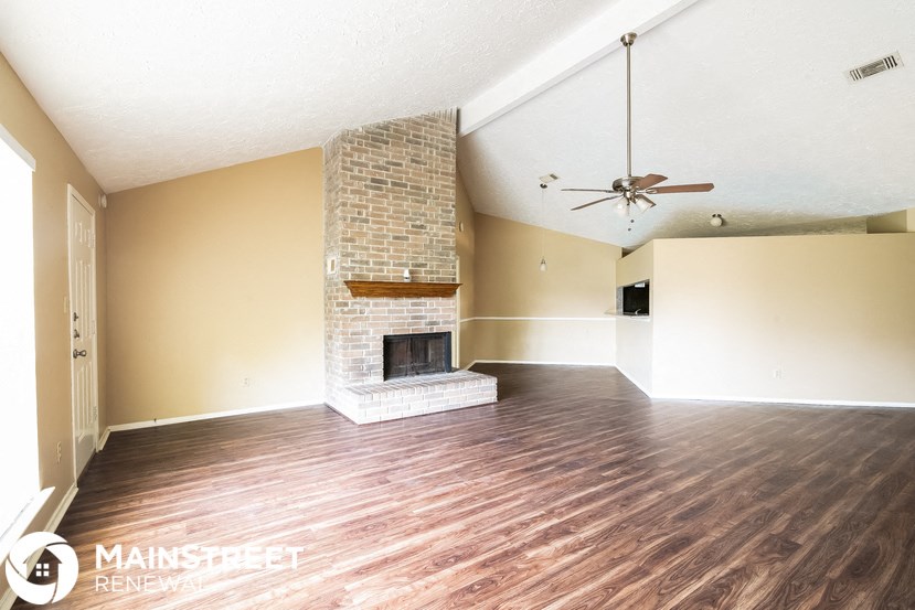 an empty living room with a brick fireplace and wooden floors