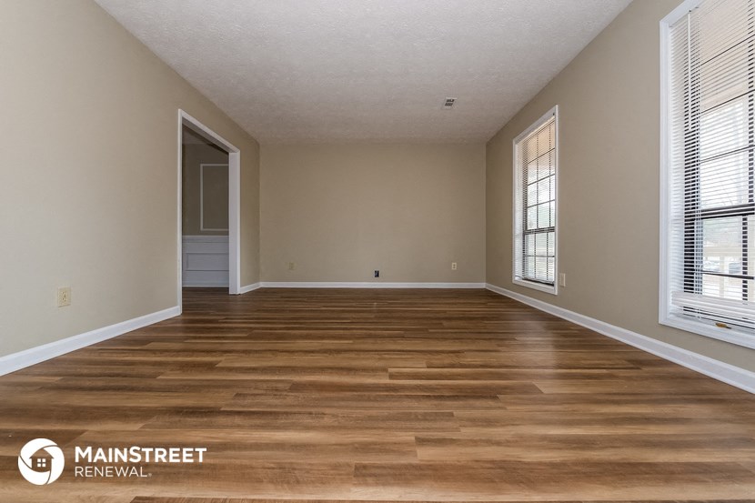 a spacious living room with wood flooring and a door to a hallway