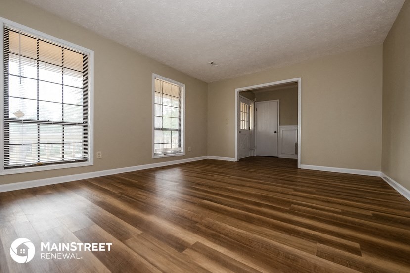 the living room of a house with wooden floors and a door to a hallway