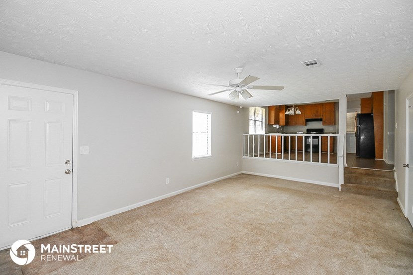 an empty living room with a ceiling fan and a kitchen