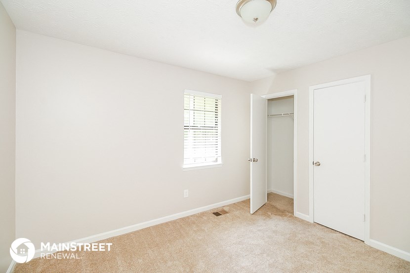 a bedroom with white walls and carpet and a door to a closet
