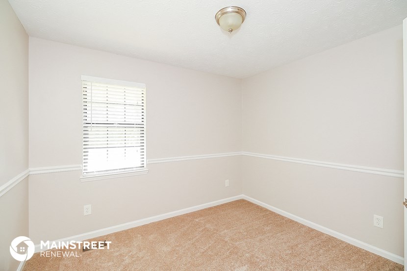 a bedroom with white walls and beige carpet and a window