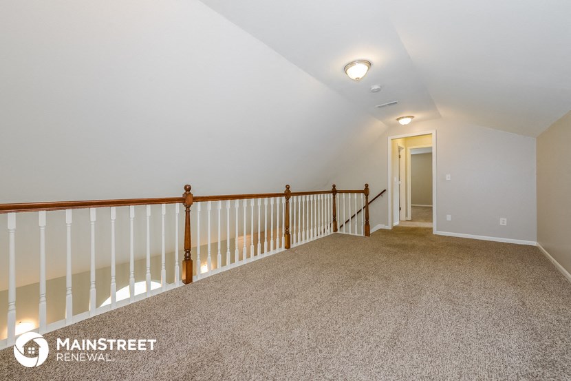 the upstairs loft has a railing and carpeted flooring and a door to the