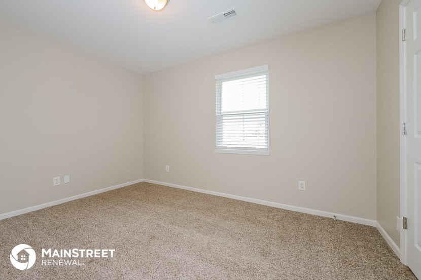 the spacious bedroom with carpeted flooring and a window