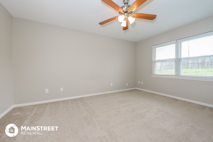 the spacious living room with ceiling fan and large window