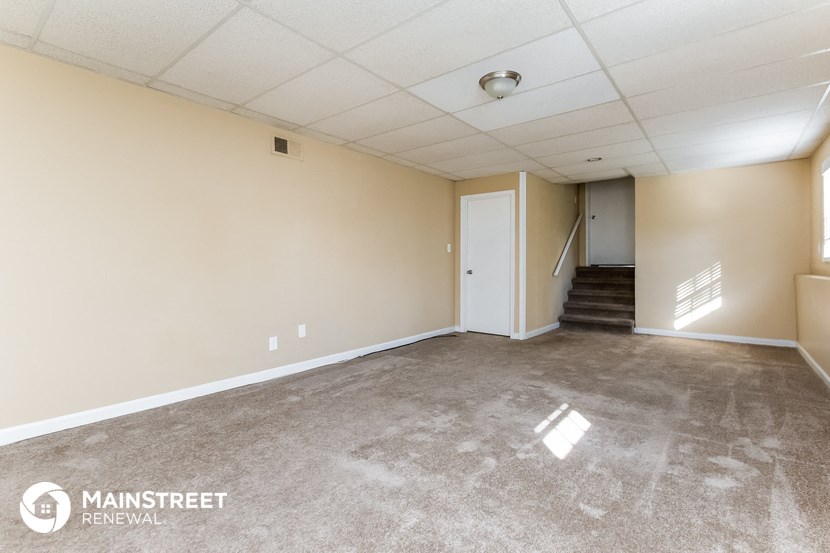 the living room of an apartment with carpeted floors and a staircase