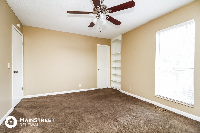 a carpeted living room with a ceiling fan and a book shelf