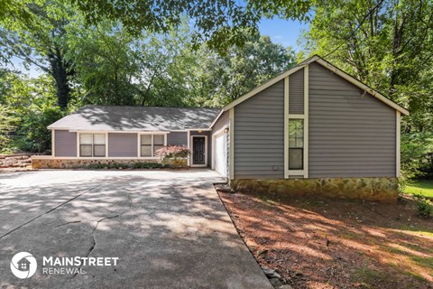 a small gray house with a driveway and trees