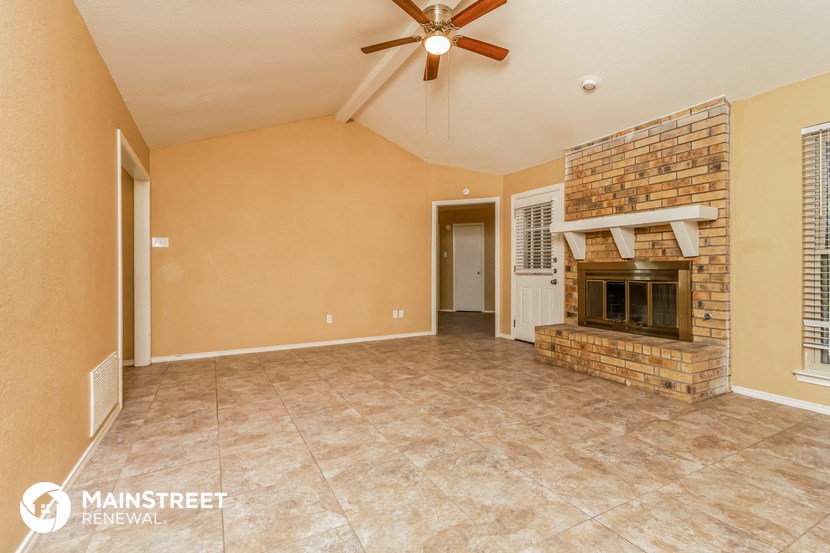 an empty living room with a brick fireplace and a ceiling fan