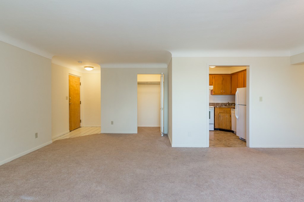 an empty living room with a kitchen in the background