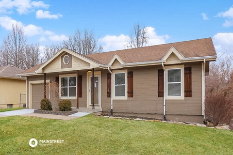 the front of a tan house with a green lawn and a blue sky