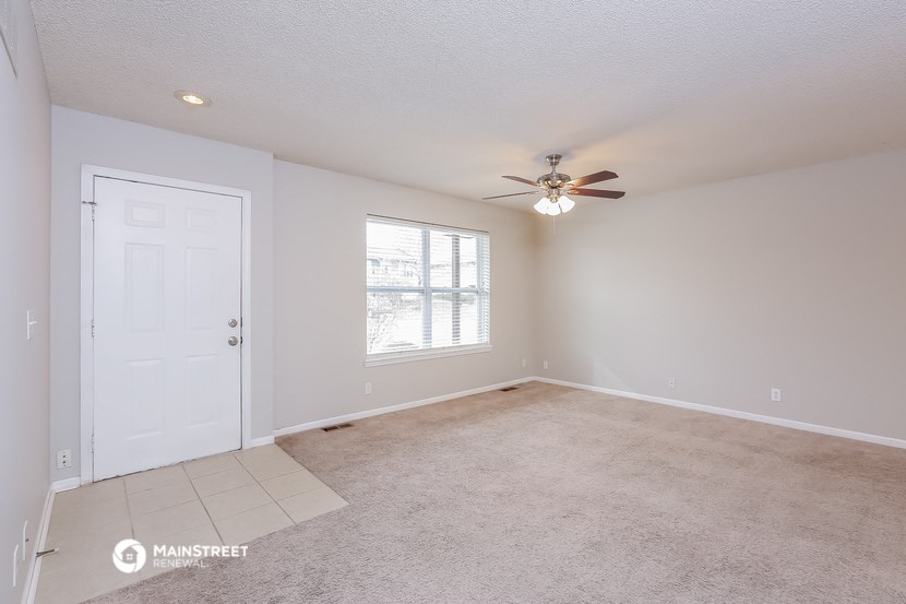 the spacious living room with ceiling fan and carpeting