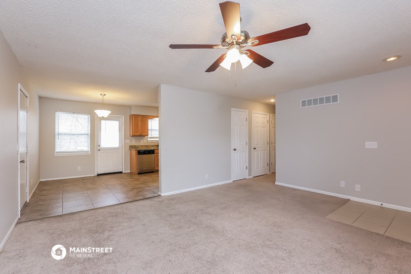 an empty living room with a ceiling fan and a kitchen
