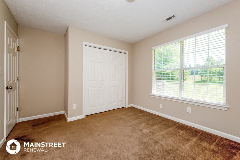 the master bedroom of this home has carpeted flooring and a large window
