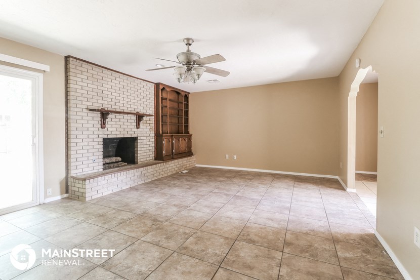 an empty living room with a brick fireplace and a ceiling fan