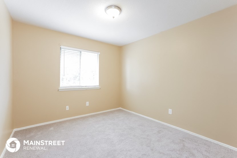 the spacious bedroom with carpeted flooring and a window