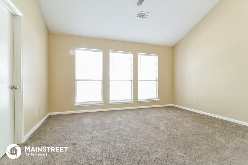 the living room of an apartment with carpet and three windows