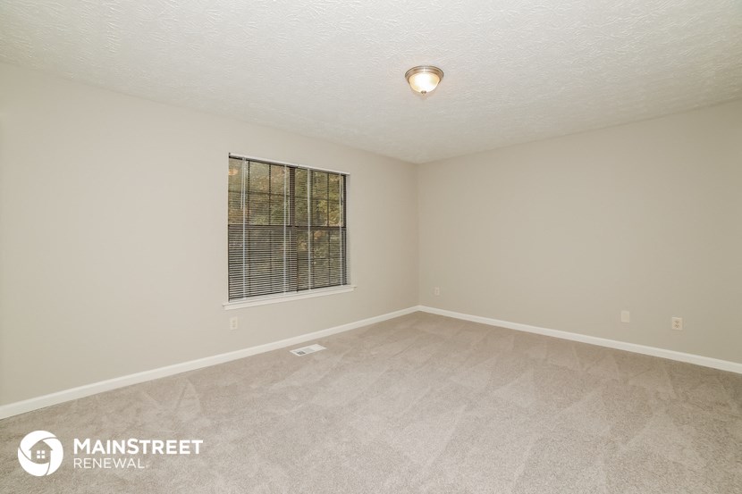 the spacious living room of this manufactured home has white carpeting and a window