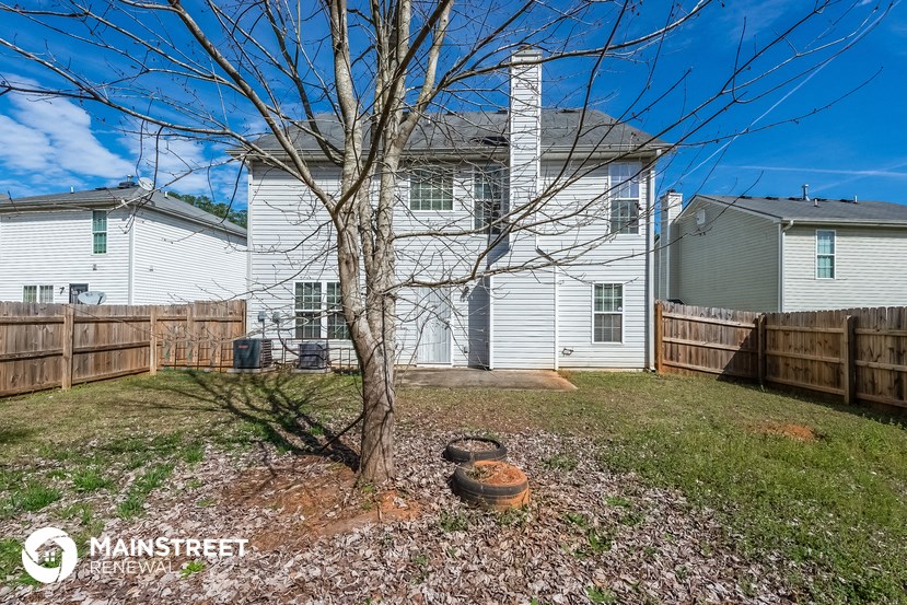 the back of a white house with a yard and a tree