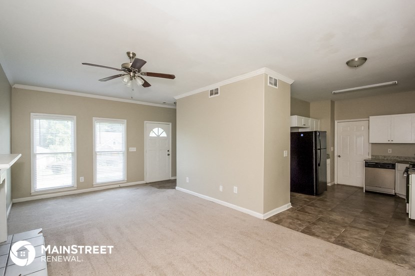 an empty living room with a ceiling fan and a kitchen