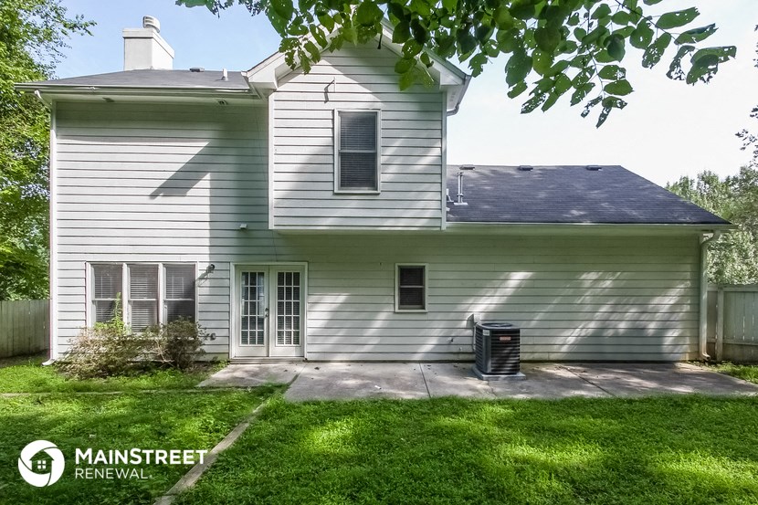 the back of a white house with a yard and a trash can