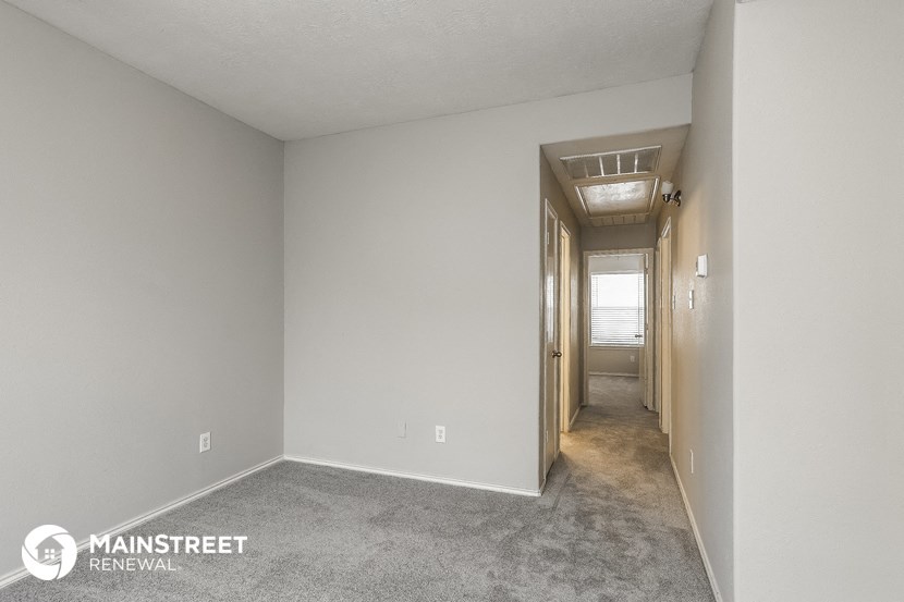 the living room and hallway of an apartment with carpet and white walls
