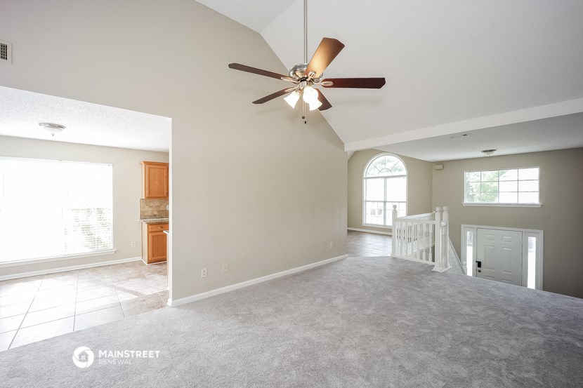 an empty living room with a ceiling fan and a staircase
