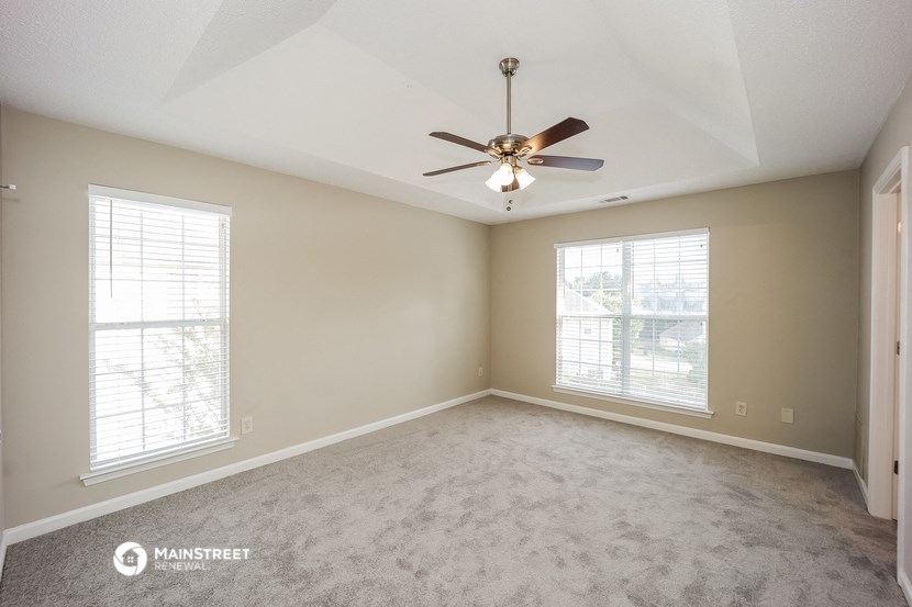 the spacious living room with ceiling fan and two windows