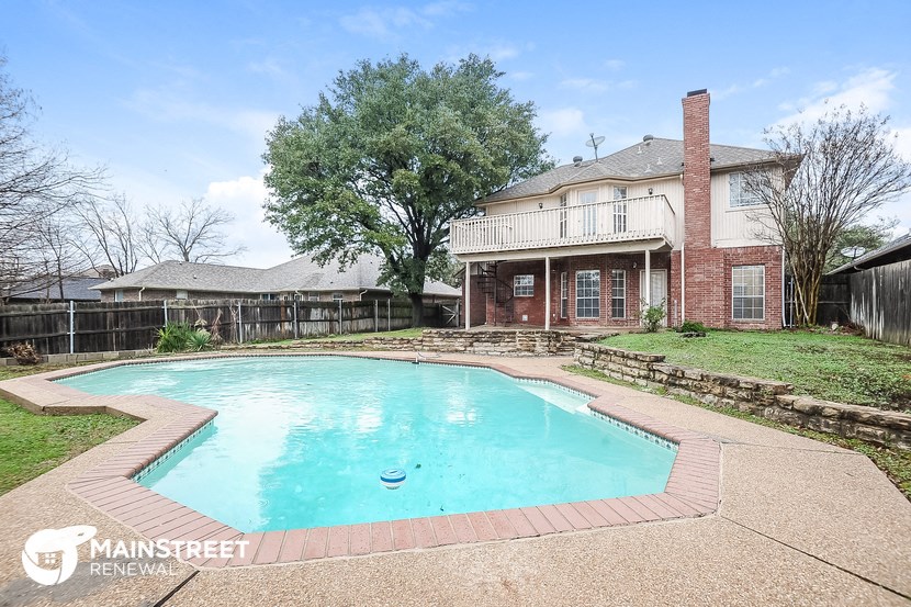 a large pool in front of a brick house with a fence