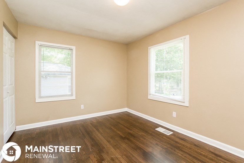 the interior of an empty room with wood flooring and two windows