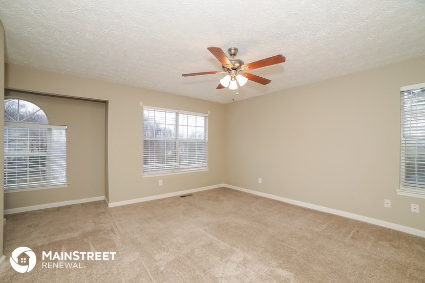 an empty living room with a ceiling fan and two windows