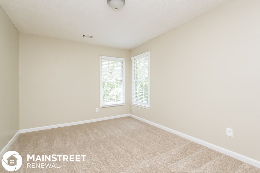 a spacious living room with carpet and two windows