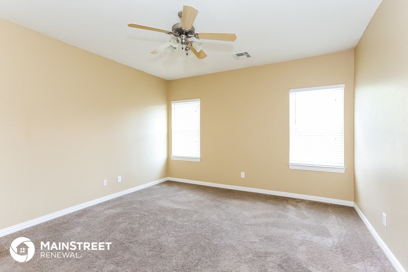 a carpeted room with a ceiling fan and two windows