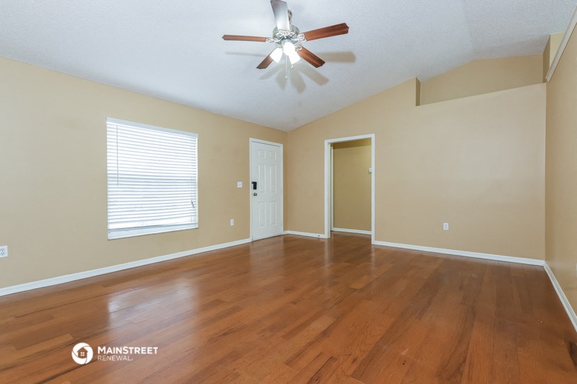 the spacious living room with hardwood floors and a ceiling fan