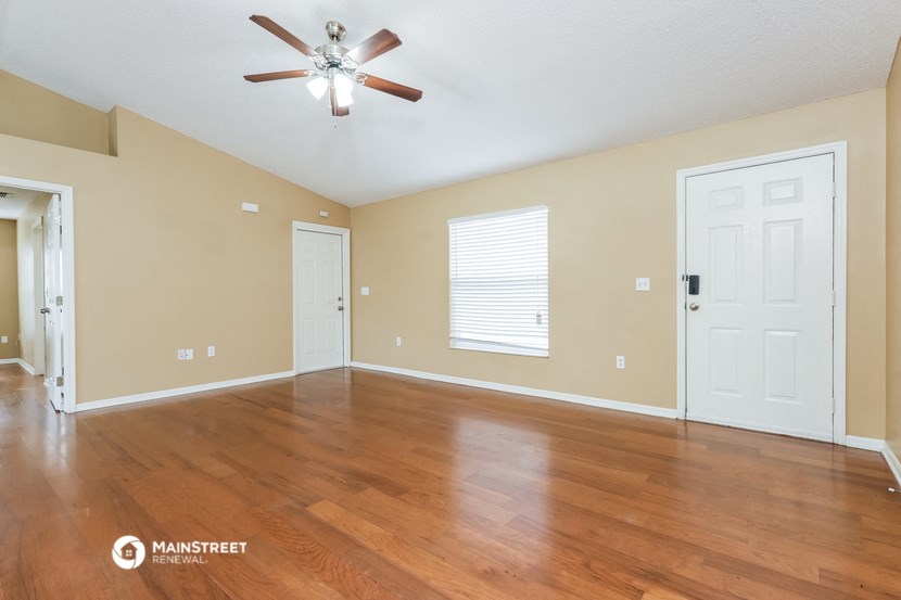 the spacious living room with hardwood floors and a ceiling fan