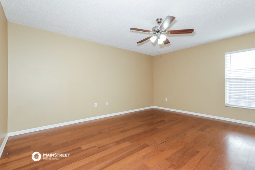 the spacious living room with hardwood floors and a ceiling fan