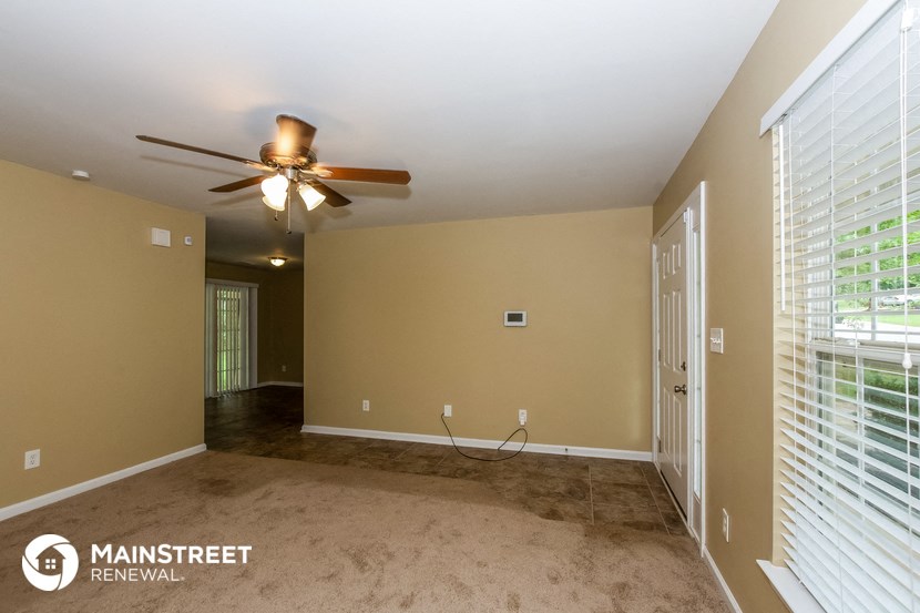 an empty living room with a ceiling fan and a door to a hallway