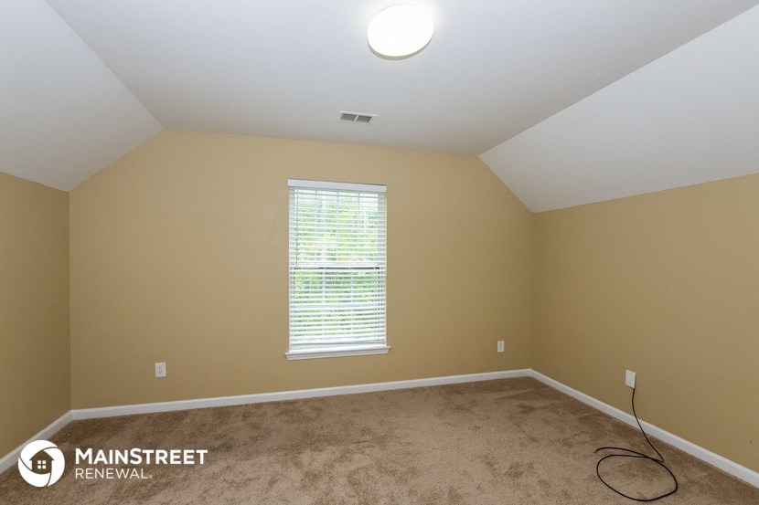 the living room of an attic with carpet and a window